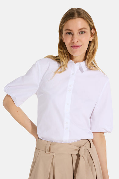 White short-sleeve button-down blouse with classic collar and puffed sleeves, worn with beige high-waisted pleated pants in a front lifestyle view.