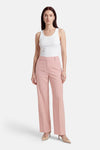 Pantalon de costume rose de MORE & MORE, coupe droite, porté avec un débardeur blanc et des escarpins nude.
