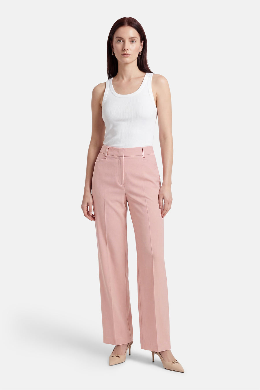 Pantalon de costume rose de MORE & MORE, coupe droite, porté avec un débardeur blanc et des escarpins nude.
