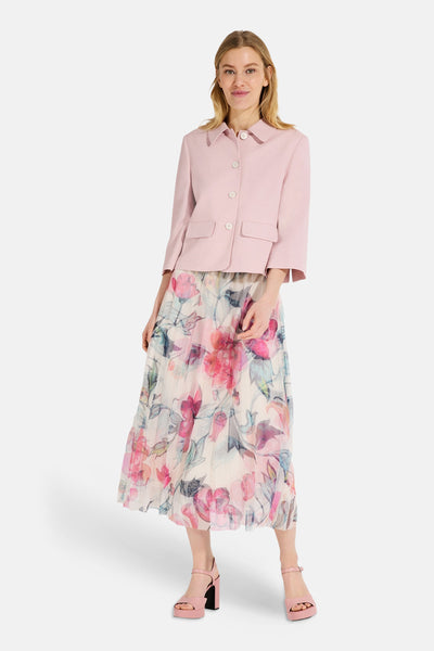 Veste courte rose de MORE & MORE avec boutons blancs, portée avec une jupe à motif floral.
