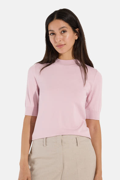Soft pink ribbed knit turtleneck sweater by MORE & MORE, short sleeves, front view on model with beige trousers.