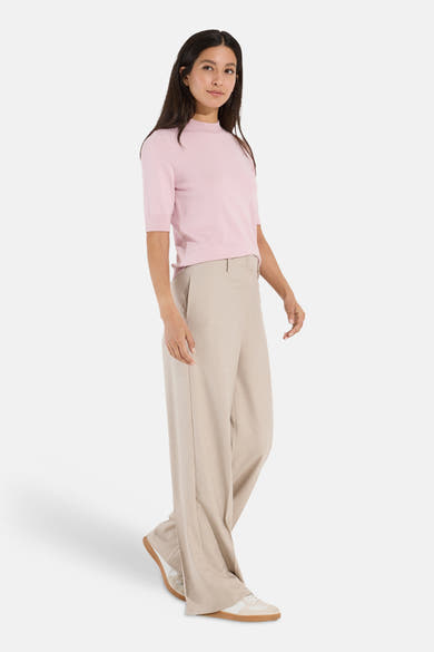 Soft pink ribbed turtleneck pullover by MORE & MORE, short sleeves, side view on model with beige wide-leg trousers and white sneakers.