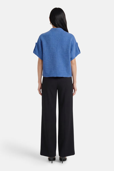 Cardigan bleu, par Terra di Siena, avec manches courtes retroussées, porté avec un pantalon noir taille haute.