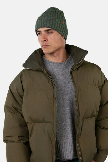 Bonnet vert de BARTS, en tricot côtelé, porté avec un pull gris et une doudoune vert olive.
