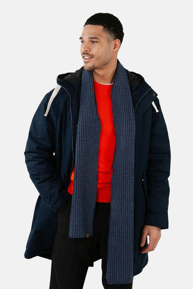 Écharpe bleue en maille côtelée de BARTS, portée avec un manteau bleu marine et un pull rouge.