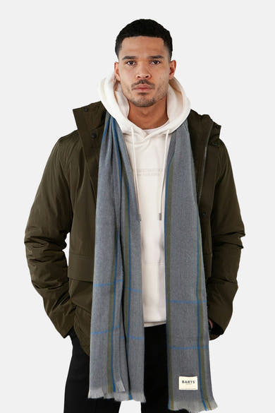 Écharpe grise à carreaux de BARTS, portée avec un sweat à capuche blanc et une veste kaki.