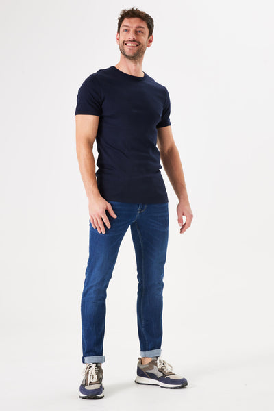 Jean slim bleu de GARCIA porté avec un t-shirt uni bleu marine et des baskets grises et bleues.