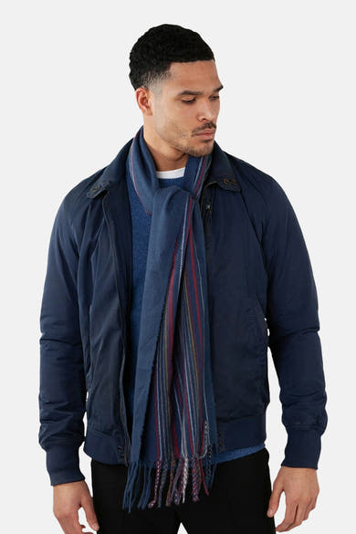 Écharpe bleue à rayures par BARTS, avec des franges et portée avec un blouson bleu marine.
