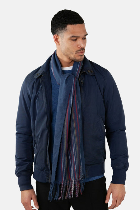 Écharpe bleue à rayures par BARTS, avec des franges et portée avec un blouson bleu marine.
