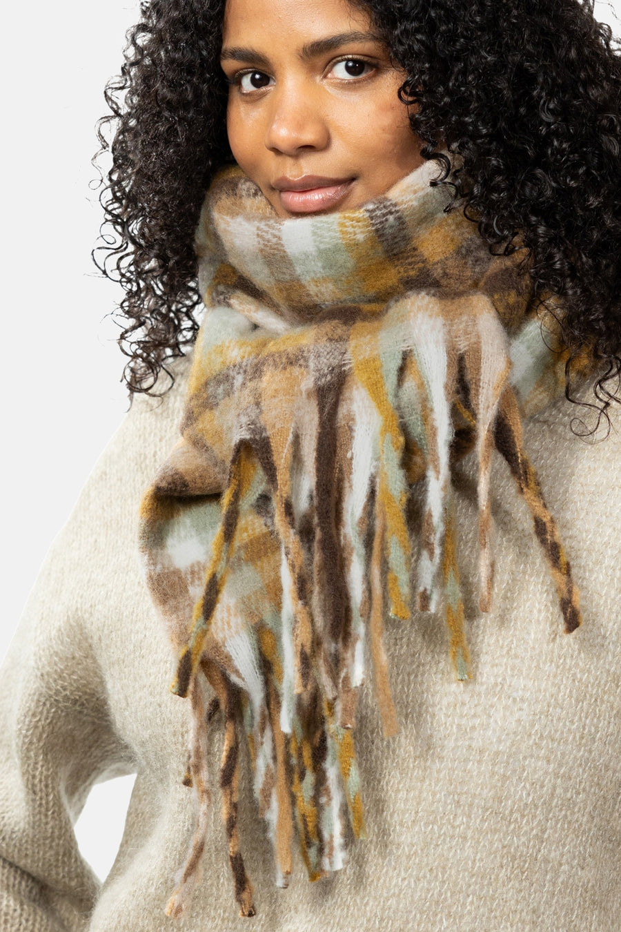 Multicolored plaid scarf with fringed edges by BARTS, worn around neck over cream knit sweater, close-up front view