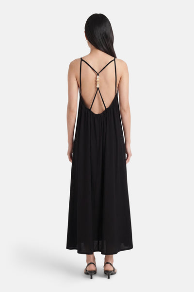 Black maxi robe with crisscross back straps and gold bead detail, shown from back view on model wearing black heels