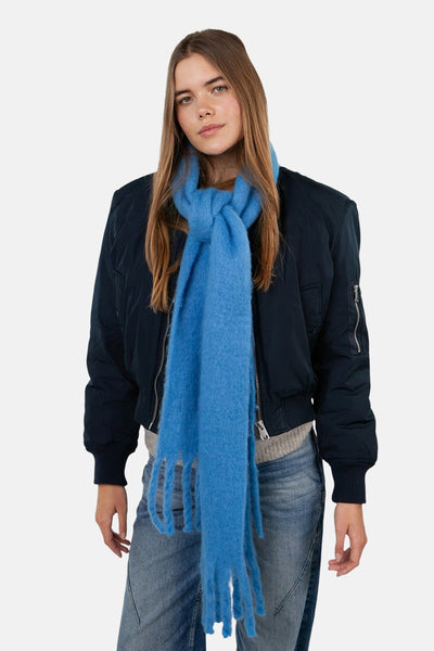 Écharpe bleue du BARTS, grosse maille duveteuse avec des franges, portée avec une veste bombardier et un jean.
