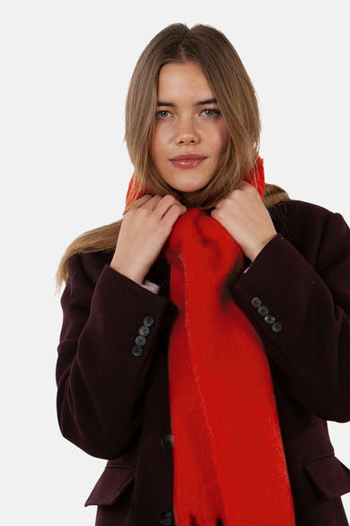 Écharpe rouge par Barts, texturée, portée avec un manteau bordeaux et des mains tenant l'écharpe.