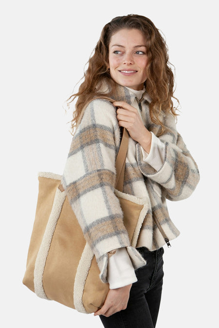 Sac à bandoulière brun de BARTS, avec bordure en fausse fourrure, porté avec une veste à carreaux et un jean noir.
