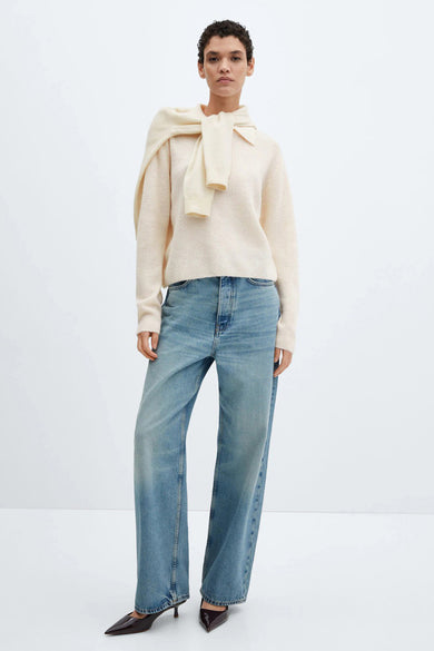 Pull beige à col rond de MANGO, porté avec un pull noué sur les épaules, et un jean taille haute.
