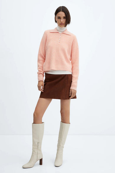 Pull rose de MANGO porté avec un col roulé, une jupe marron et des bottes montantes couleur crème.
