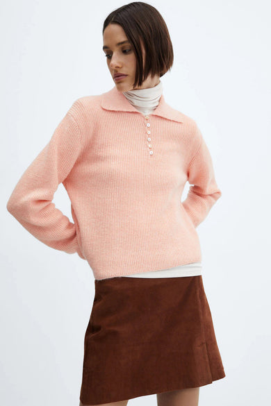Pull rose de MANGO, porté sur un col roulé crème et une jupe courte marron.