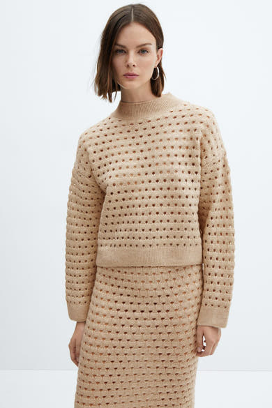 Beige trui van MANGO, met ajourpatroon, gedragen met een bijpassende rok en oorringen.