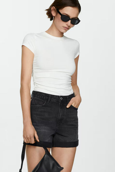 Short en denim noir de MANGO, porté avec un t-shirt blanc et des lunettes de soleil.