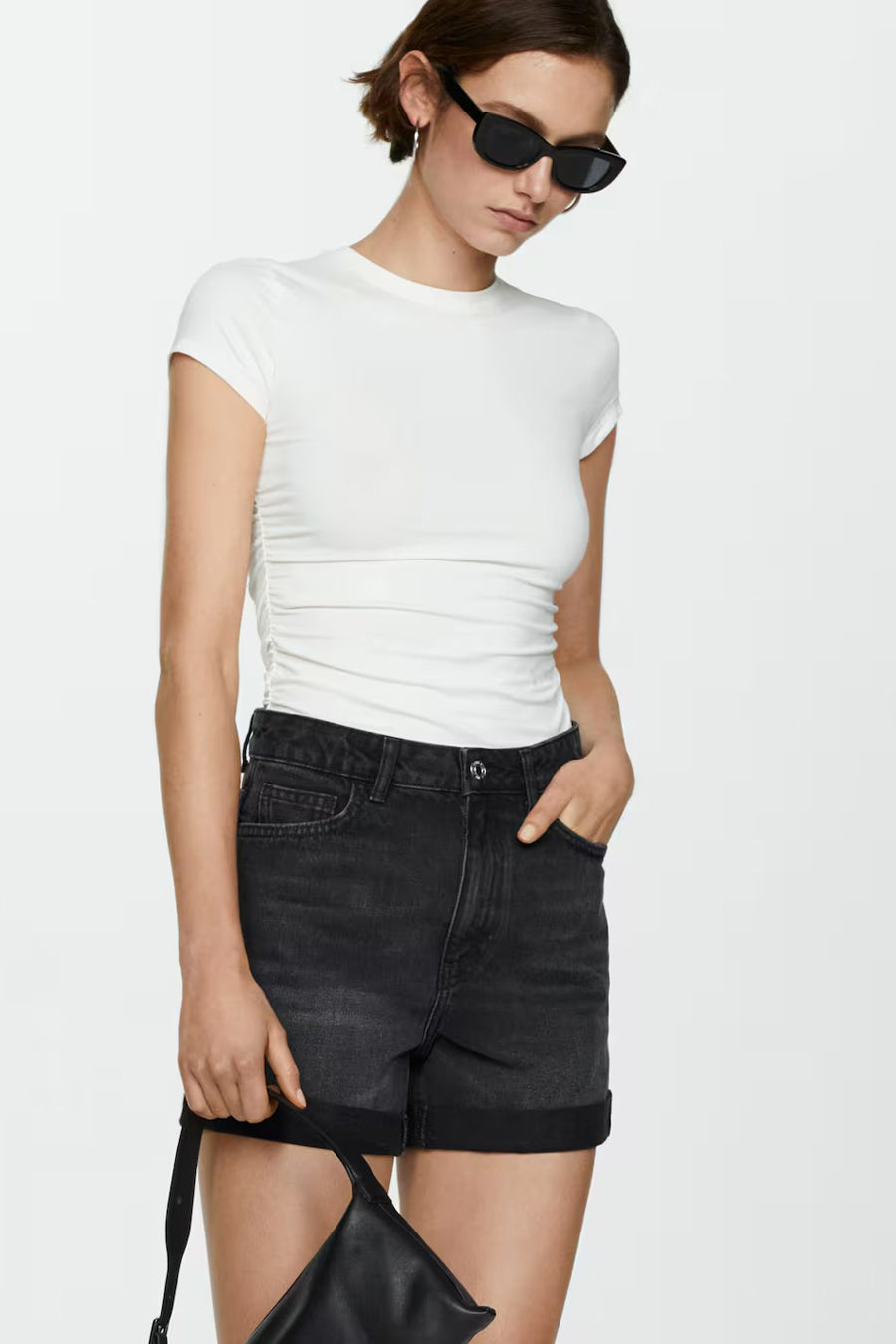 Short en denim noir de MANGO, porté avec un t-shirt blanc et des lunettes de soleil.