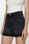 Short en denim noir de MANGO, avec ourlets revers et porté avec un t-shirt blanc moulant.