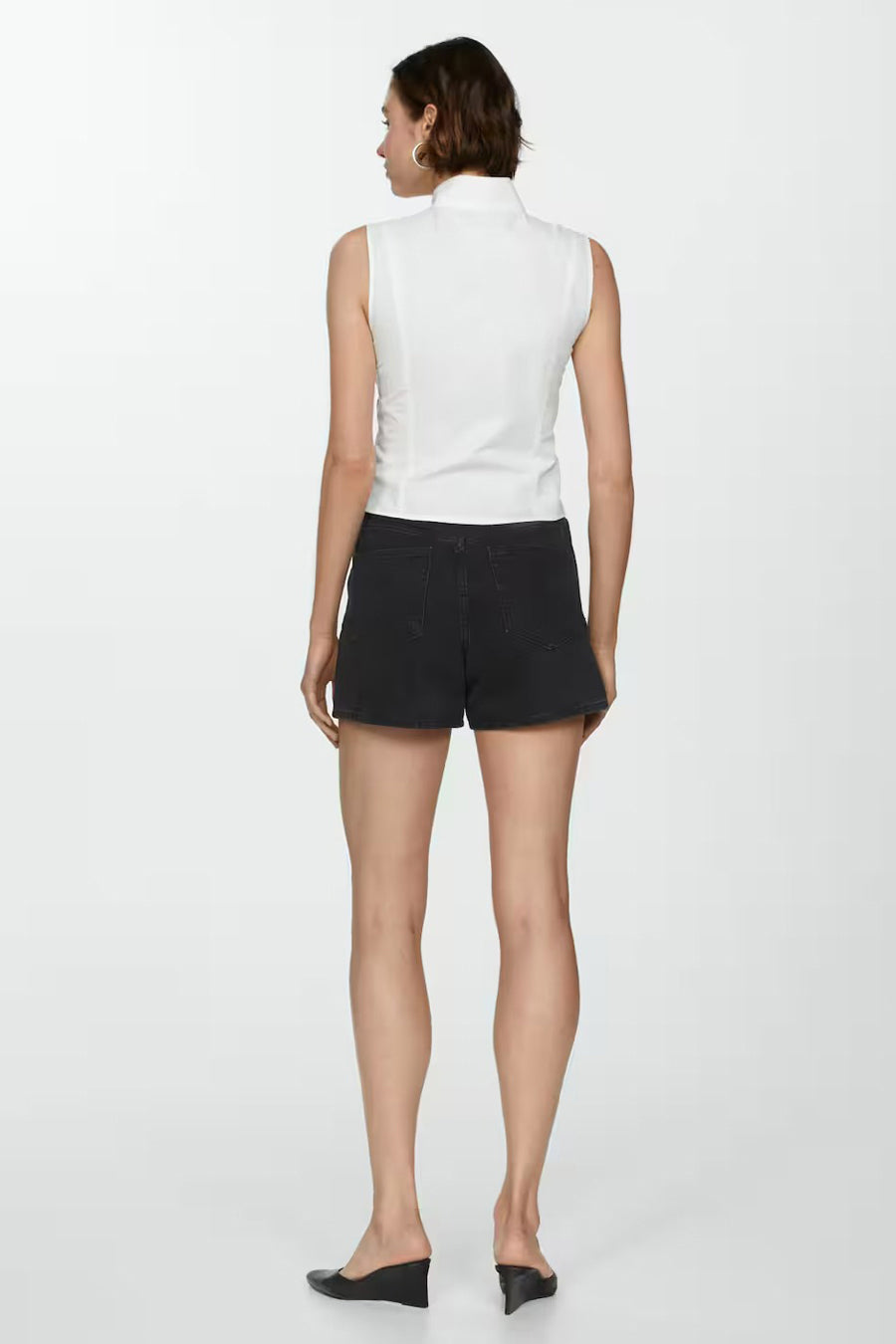 Short noir de MANGO, porté avec un haut blanc sans manches et des chaussures compensées noires.