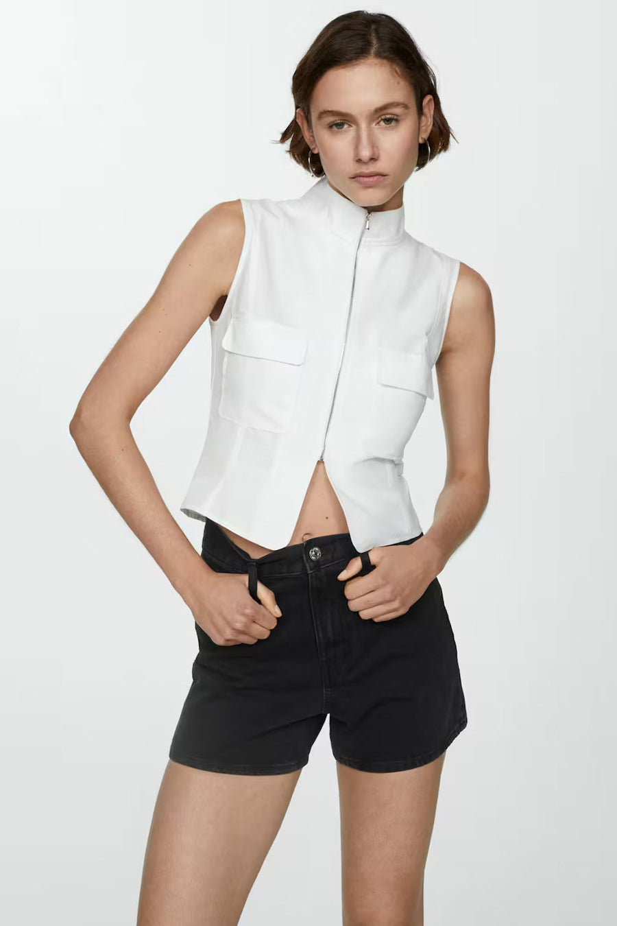 Zwarte korte broek van MANGO, gedragen met een mouwloze witte top en de handen in de zakken.