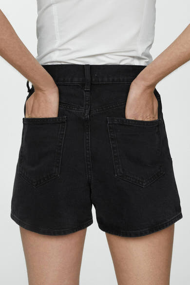 Korte zwarte broek van MANGO, met zichtbare achterzakken, gedragen met een effen wit T-shirt, handen in de zakken.