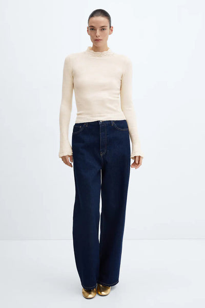 Pull beige à col montant par MANGO, avec détails en dentelle au col et poignets, porté avec un jean bleu et des ballerines dorées.