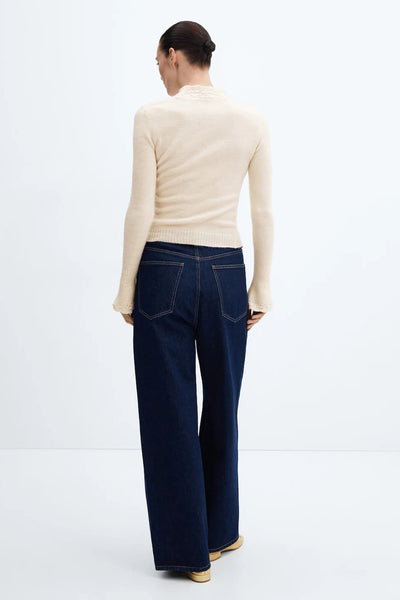 Pull beige van MANGO, coupe ajustée, avec détails ajourés à l'encolure et aux poignets, porté avec un jean taille haute foncé.

