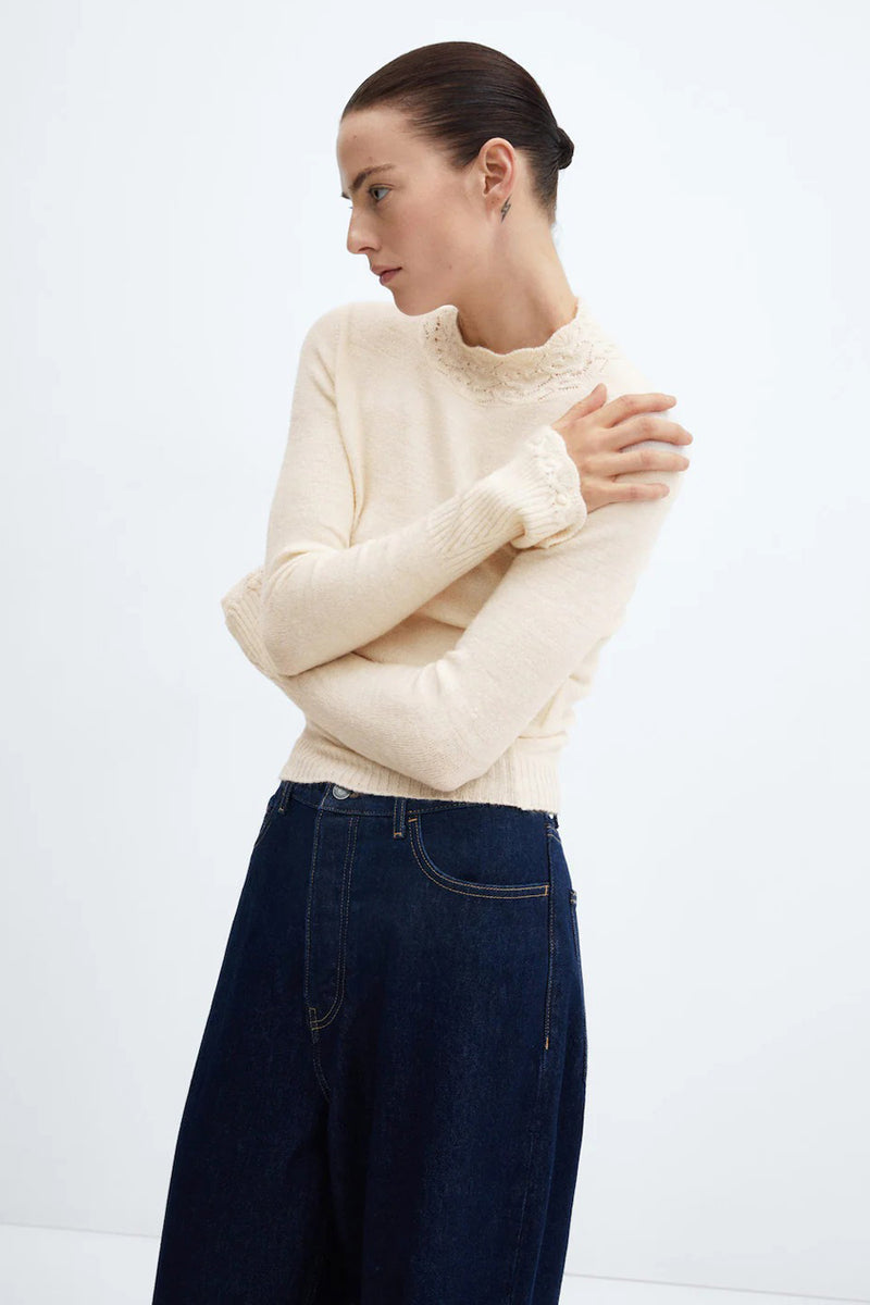 Pull beige à col montant de MANGO, détails ajourés à l'encolure, porté avec un jean taille haute.