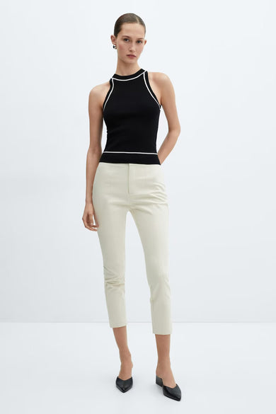 Black halter-neck tank top with white trim by MANGO, worn with cream trousers and black heels, front view.