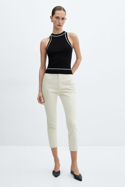 Black halter-neck tank top with white trim by MANGO, worn with cream trousers and black heels, front view.