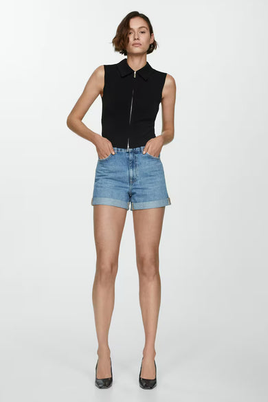 Short en denim bleu clair de MANGO, avec ourlets retroussés et porté avec un haut noir à fermeture éclair.
