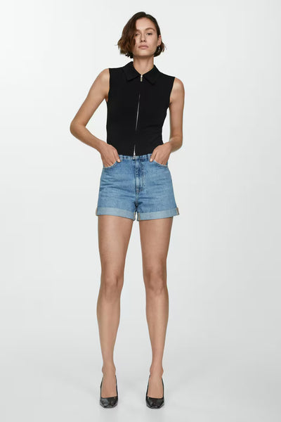 Short en denim bleu clair de MANGO, avec ourlets retroussés et porté avec un haut noir à fermeture éclair.
