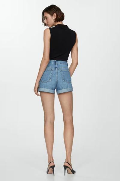 Short en denim bleu clair de MANGO, avec ourlets roulés, porté avec un haut noir et des talons aiguilles.