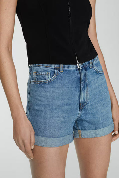 Short en denim bleu de MANGO, avec ourlet retroussé et fermeture éclair visible.