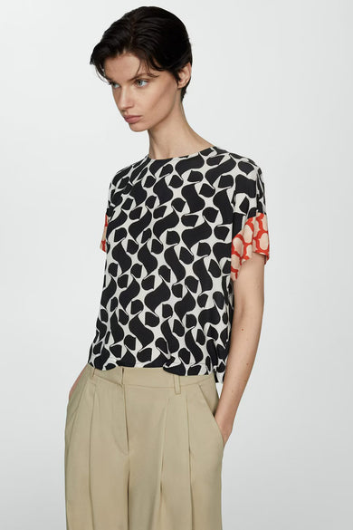 Blouse à manches courtes multicolore de MANGO, avec motif abstrait noir et blanc et manches à pois rouges.
