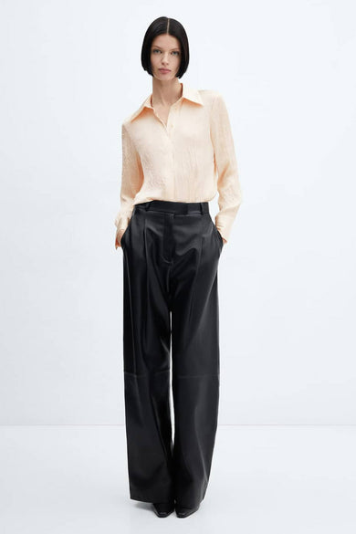 Chemisier beige à manches longues de MANGO, avec une subtile texture florale, porté avec un pantalon noir ample.
