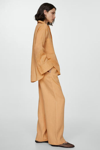 Chemise orange à manches longues de MANGO, portée avec un pantalon ample de la même couleur et des chaussures à mailles.