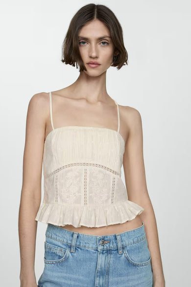 Blouse beige sans manches de MANGO, avec broderie florale et bordure en dentelle, portée avec un jean taille basse.
