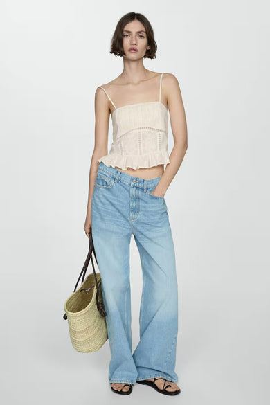 Blouse sans manches beige de MANGO, avec détails en dentelle et volant, portée avec un jean bleu ample.
