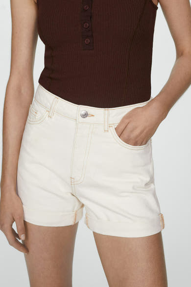 Short beige de MANGO avec coutures contrastées et ourlets retroussés, porté avec un haut marron côtelé.