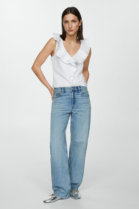 White sleeveless top with ruffled V-neck and shoulder details, worn with light blue jeans and silver flats, front view.