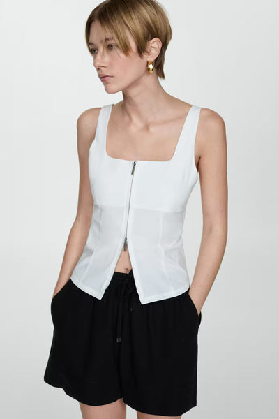 Short noir de MANGO, porté avec un haut blanc à fermeture éclair et des boucles d'oreilles dorées.
