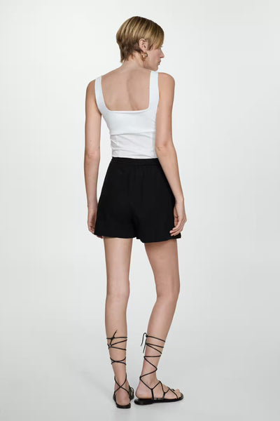 Zwarte korte broek van MANGO, gedragen met een witte top en sandalen met bandjes die om de enkels zijn gewikkeld.