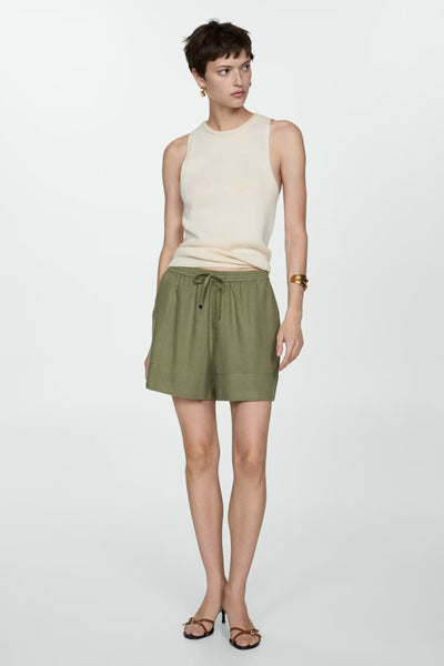 Short kaki en lin de MANGO, avec cordon de serrage à la taille, porté avec un top et des sandales à talons.
