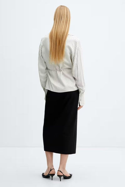 Chemisier beige à rayures de MANGO, porté avec une jupe noire midi et des chaussures à talons noirs.