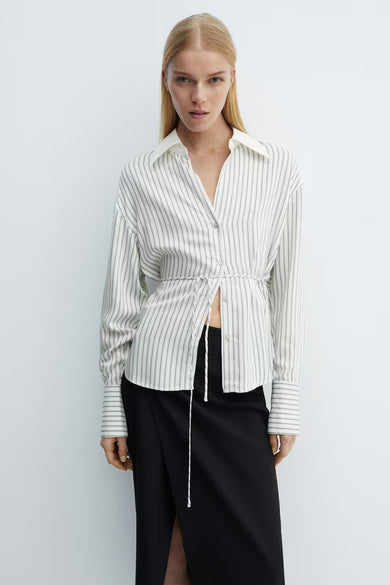 Chemise beige rayée à manches longues de MANGO, avec cordon de serrage et jupe noire fendue.