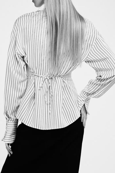 Beige lange mouwen blouse van MANGO, zwarte verticale strepen, gestrikt aan de taille, gedragen met een zwarte rok.